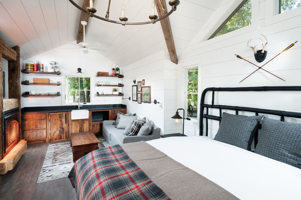 A studio room has a black iron bed decorated with warm cozy sheets with a couch sitting in front of a fireplace.