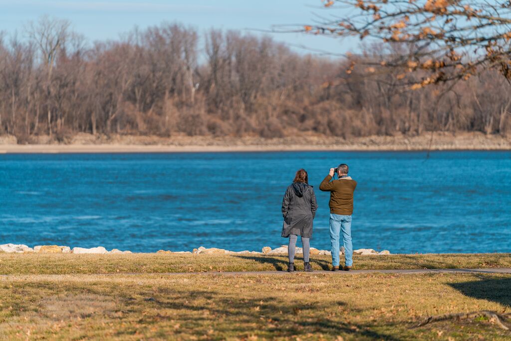 Two people stand at edge of river and look towards the sky in hopes of seeing an eagle.