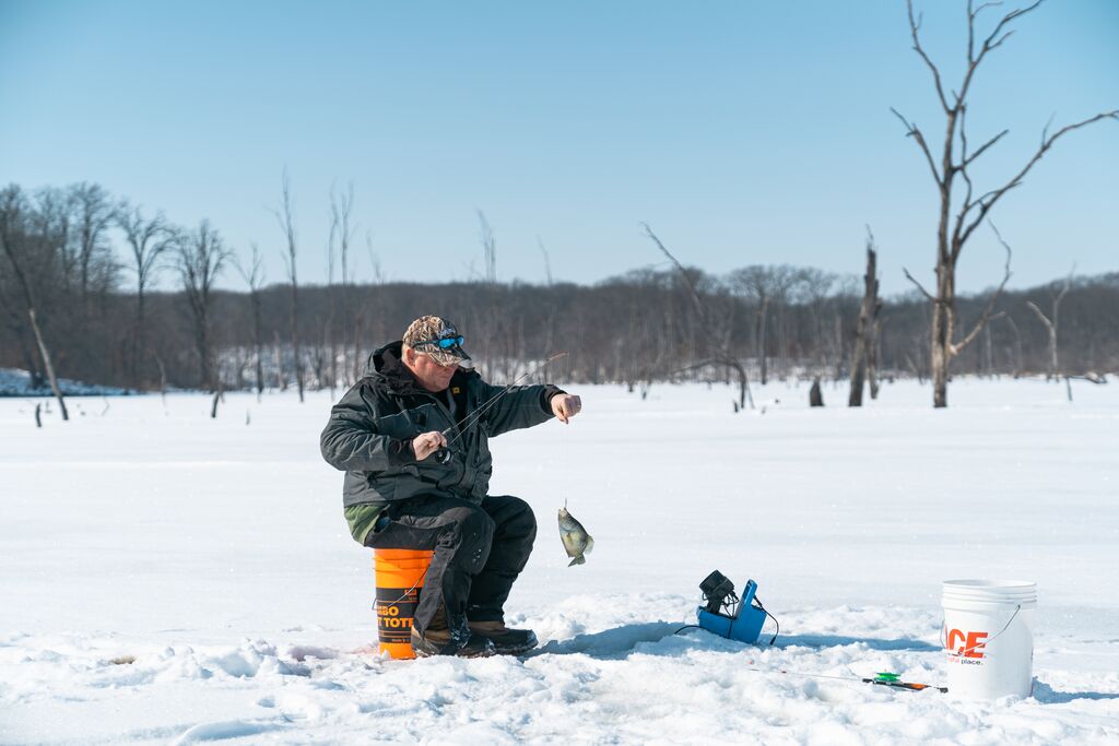 Person ice fishing on lake and has a fish on the line.