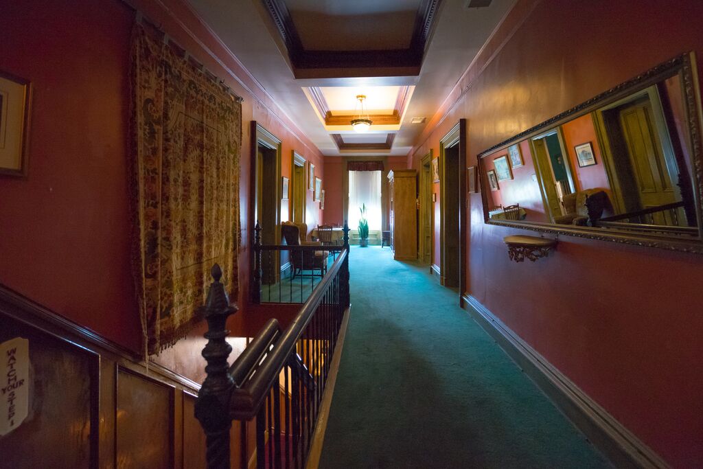 A hallway with dark burgundy walls and turquoise carpet. The hallway leads to an ominously lit window at the end of the hall.