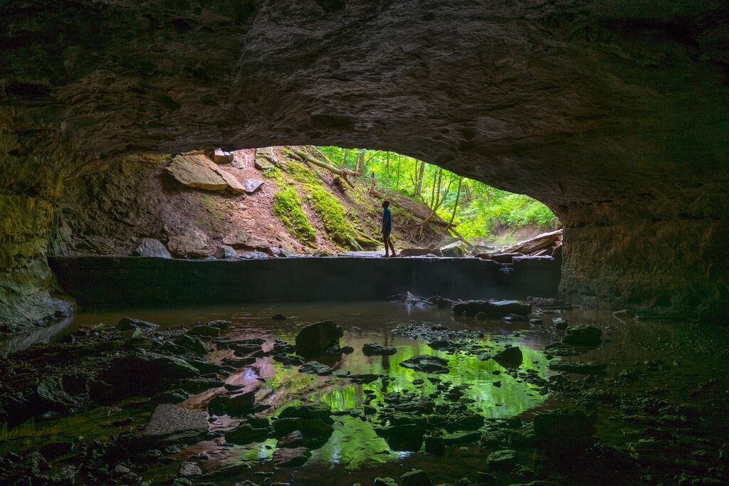 A person stands under a natural bridge formation.