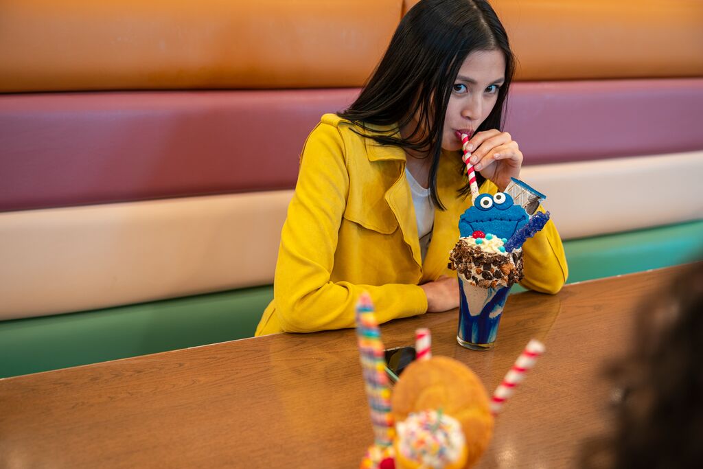 A young woman drinks a cookie monster themed shake with cookie pieces, candy and a striped straw.