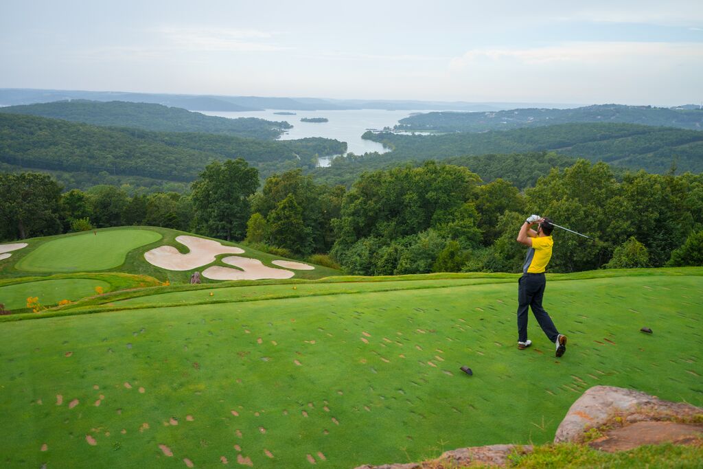 Person tees off at golf course with vistas of Table Rock Lake and the Ozark Mountains